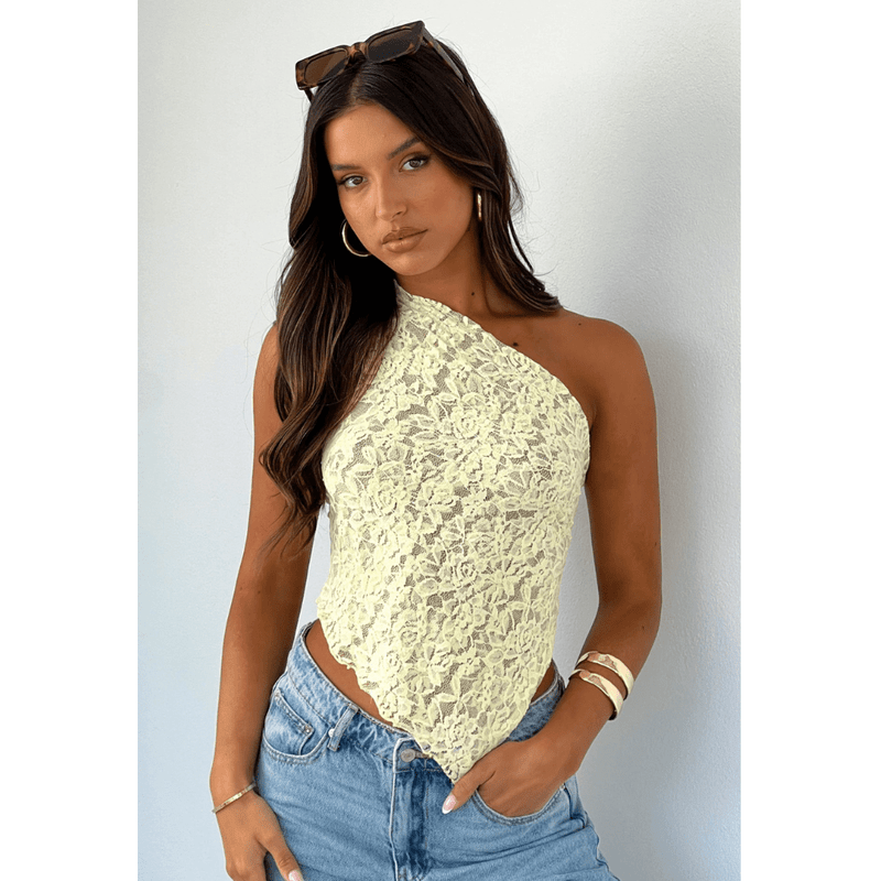 Frau trägt ein elegantes One-Shoulder-Spitzentop in zartem Hellgelb mit asymmetrischem Schnitt – ein femininer Sommerlook für entspannte Tage oder stylishe Festival-Momente.