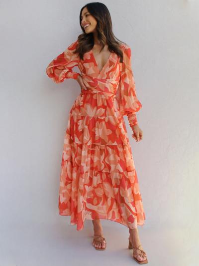 Frau trägt ein oranges Maxikleid mit Blumenmuster, langen Puffärmeln, V-Ausschnitt, geraffter Taille und Stufenrock, kombiniert mit Absatzsandalen